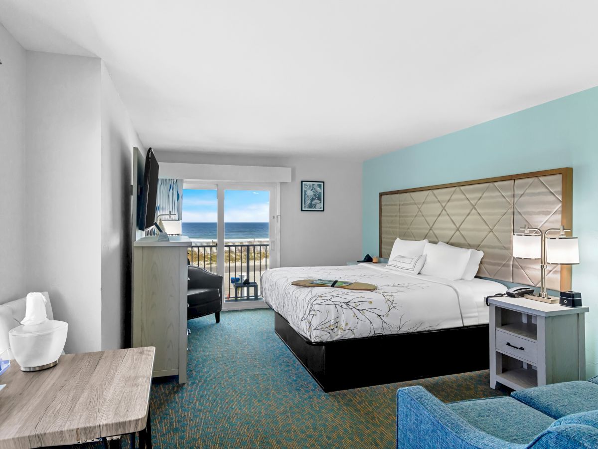 A hotel bedroom with a large bed, bedside lamps, ocean view balcony doors, and a small bathroom area with a toilet.