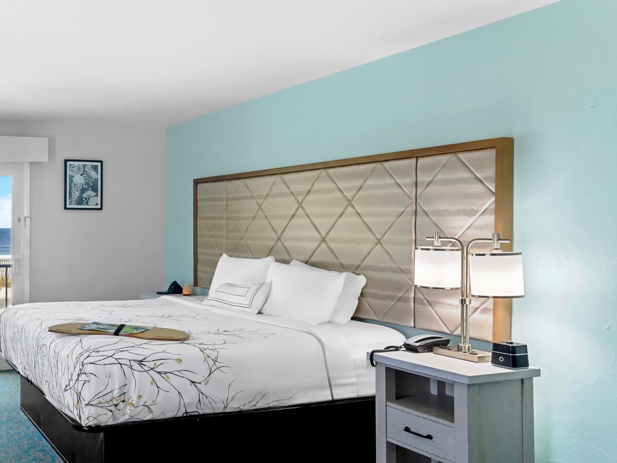 A modern hotel bedroom with a king bed, tufted headboard, blue walls, and a bedside table with lamps.