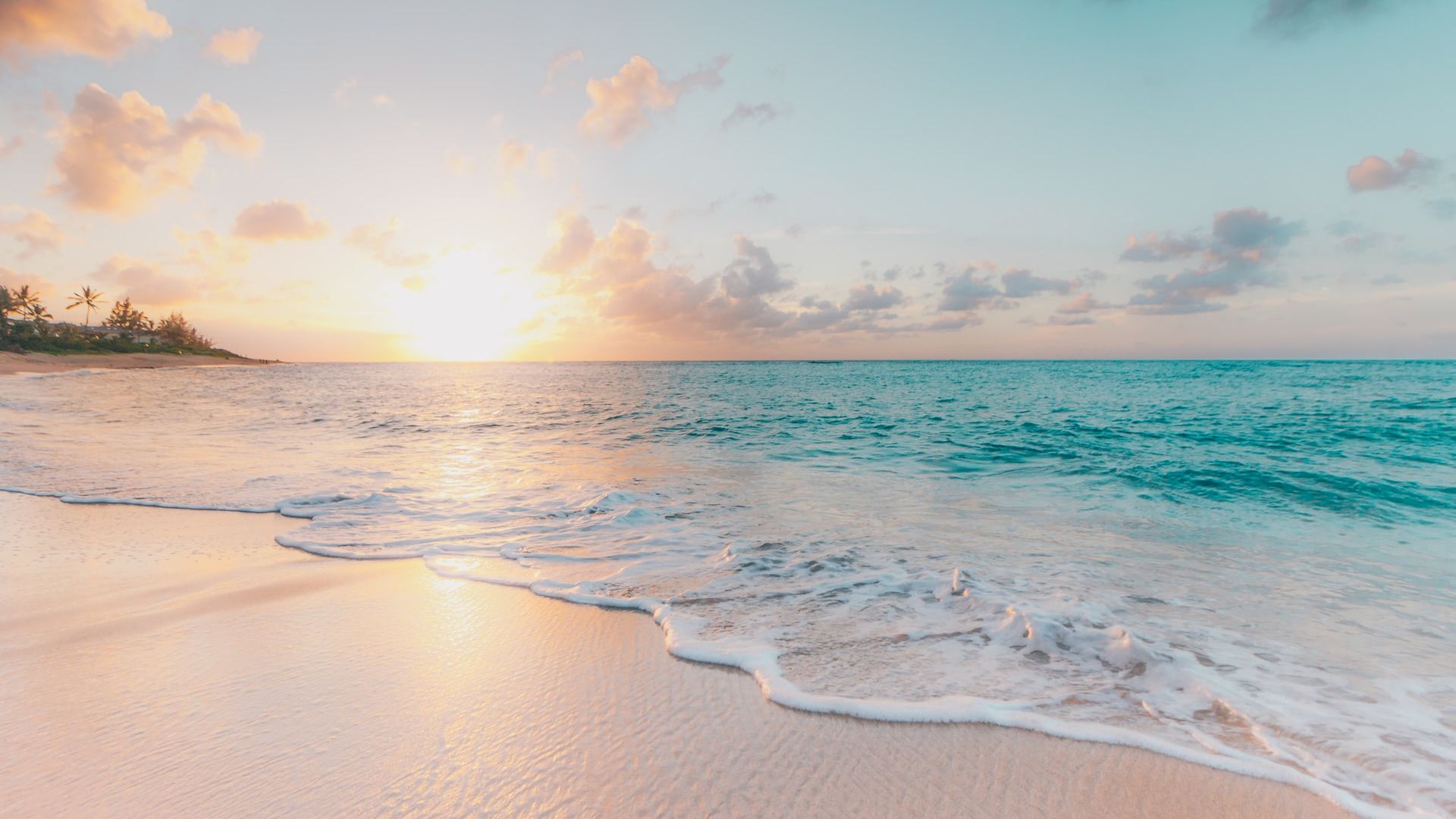 A serene beach scene with gentle waves, soft sand, and a vibrant sunset casting warm colors on the water and sky.