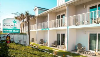 The image shows a two-story hotel with balconies and a sign reading "Boutique Inn" and "Private Beach" next to palm trees and patio seating.