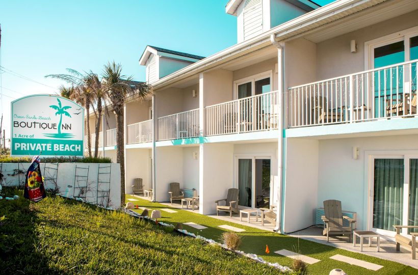 The image shows a two-story hotel with balconies and a sign reading "Boutique Inn" and "Private Beach" next to palm trees and patio seating.