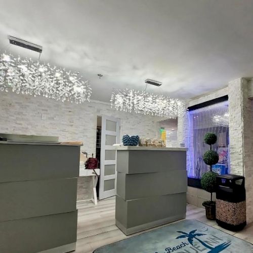 A modern reception area with decorative lighting, two desks, plants, and rugs with a palm tree design.