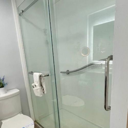 The image shows a modern bathroom with a glass-enclosed shower, a toilet, and a small potted plant on the toilet tank.