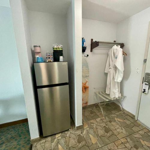 The image shows a hotel room entry with a mini-fridge, some drinks on top, and robes hanging on a rack next to the door.