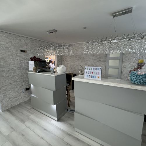 A modern reception area with gray desks, lighted sign, decorative crystal strings, flowers, and a stack of blue paper towels on the counter.