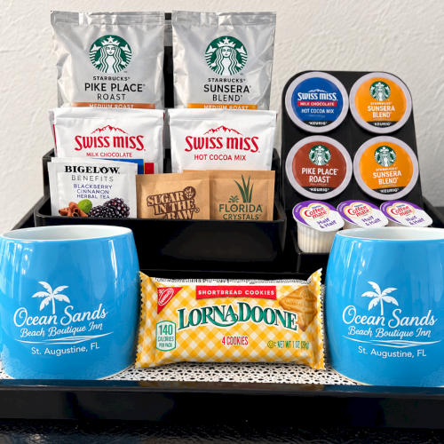 A tray gift set with Starbucks/Sixss Miss cocoa, coffee pods, Florida crystals, shortbread cookies, and two blue &ldquo;Ocean Sands&rdquo; mugs.