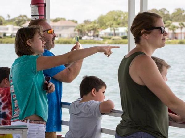 A group of people on a boat, with some pointing and looking out over the water, seemingly engaged in sightseeing or enjoying the view.