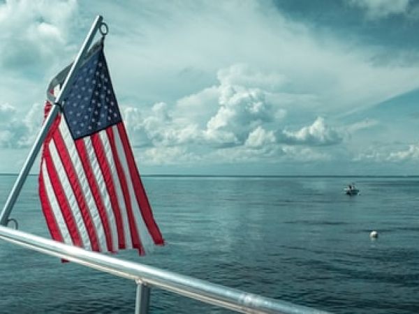 An American flag on a boat against a calm sea and cloudy sky backdrop, with another boat visible in the distance.