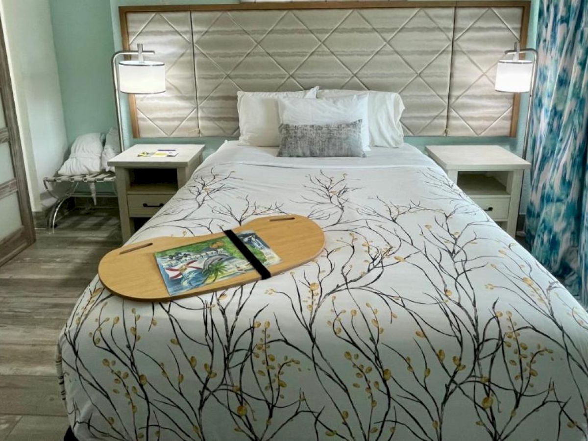 A neatly made bed with a decorative headboard, two nightstands with lamps, and a wooden tray with a book on the bedspread.